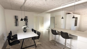 A modern kitchen with a white countertop, black bar stools, and pendant lighting.