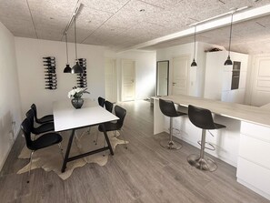 Et moderne køkken med hvid bordplade, sorte barstole og hængende lamper.