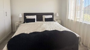 A bedroom with a bed, two bedside tables, a wardrobe, and a window with curtains.