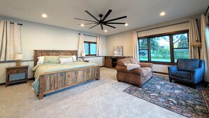 A bedroom with a wooden bed, a ceiling fan, a large window, and a view of the outdoors.