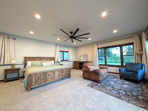 A bedroom with a wooden bed, a ceiling fan, a large window, and a view of the outdoors.