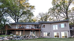 A two-story house with a balcony, large windows, and a stone wall.