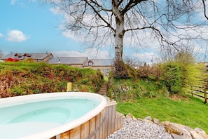 A wooden hot tub in a garden with a tree, stone wall, and a building in the background. - Jasper, Kiri & Norton - joint booking (Dulverton)