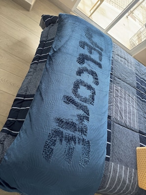 Une pièce avec un lit, une fenêtre et un oreiller bleu à motifs.