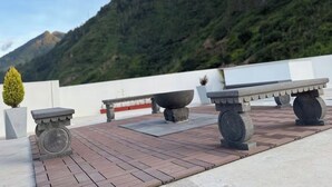 Une terrasse sur le toit, agrémentée de tables en pierre et de jardinières, offrant une vue sur un paysage montagneux.
