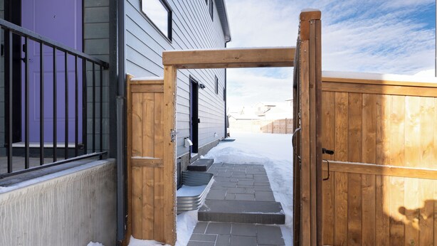 A snow-covered pathway leading to a wooden gate, a purple door, and a house with a visible window and door. - New 2 bed, 1 bathroom apartment (Calgary)