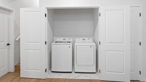 A laundry room with two white front-loading washers and dryers, white walls, and a wooden floor. - New 2 bed, 1 bathroom apartment (Calgary)