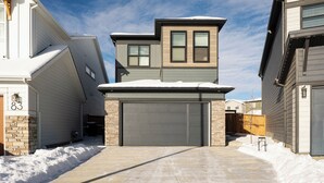 A residential driveway leading to a garage with a snow-covered roof and a two-story house with a visible garage door number 87. - New 2 bed, 1 bathroom apartment (Calgary)