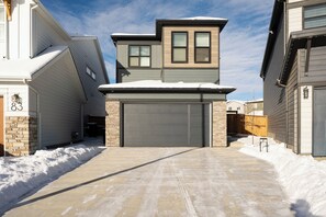 Ein Auffahrt führt zu einer Garage mit einem mit Schnee bedeckten Dach und einem zweistöckigen Haus, dessen Garagenummer 87 sichtbar ist.