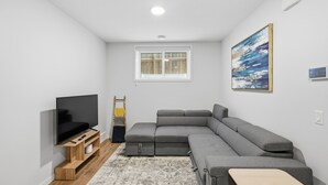 A modern living room with a sectional sofa, a flat-screen TV, a wooden TV stand, a small table, a patterned rug, and a painting on the wall. - New 2 bed, 1 bathroom apartment (Calgary)