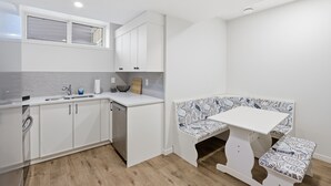 A compact kitchen with white cabinetry, a built-in dishwasher, and a small dining area with a bench and table. - New 2 bed, 1 bathroom apartment (Calgary)