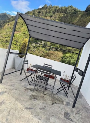 An outdoor patio with a table and chairs, a pergola, and a view of a mountainous landscape. - Airbnb La Paz (Baños de Agua Santa)