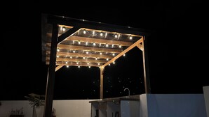 En uteplats med en pergola av trä, ljusslingor och en inbyggd grill.