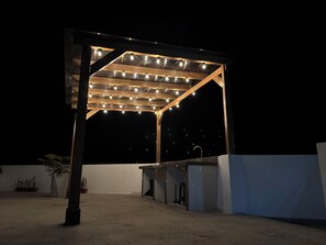 An outdoor patio with a wooden pergola structure, string lights, and a built-in barbecue grill. - Airbnb La Paz (Baños de Agua Santa)