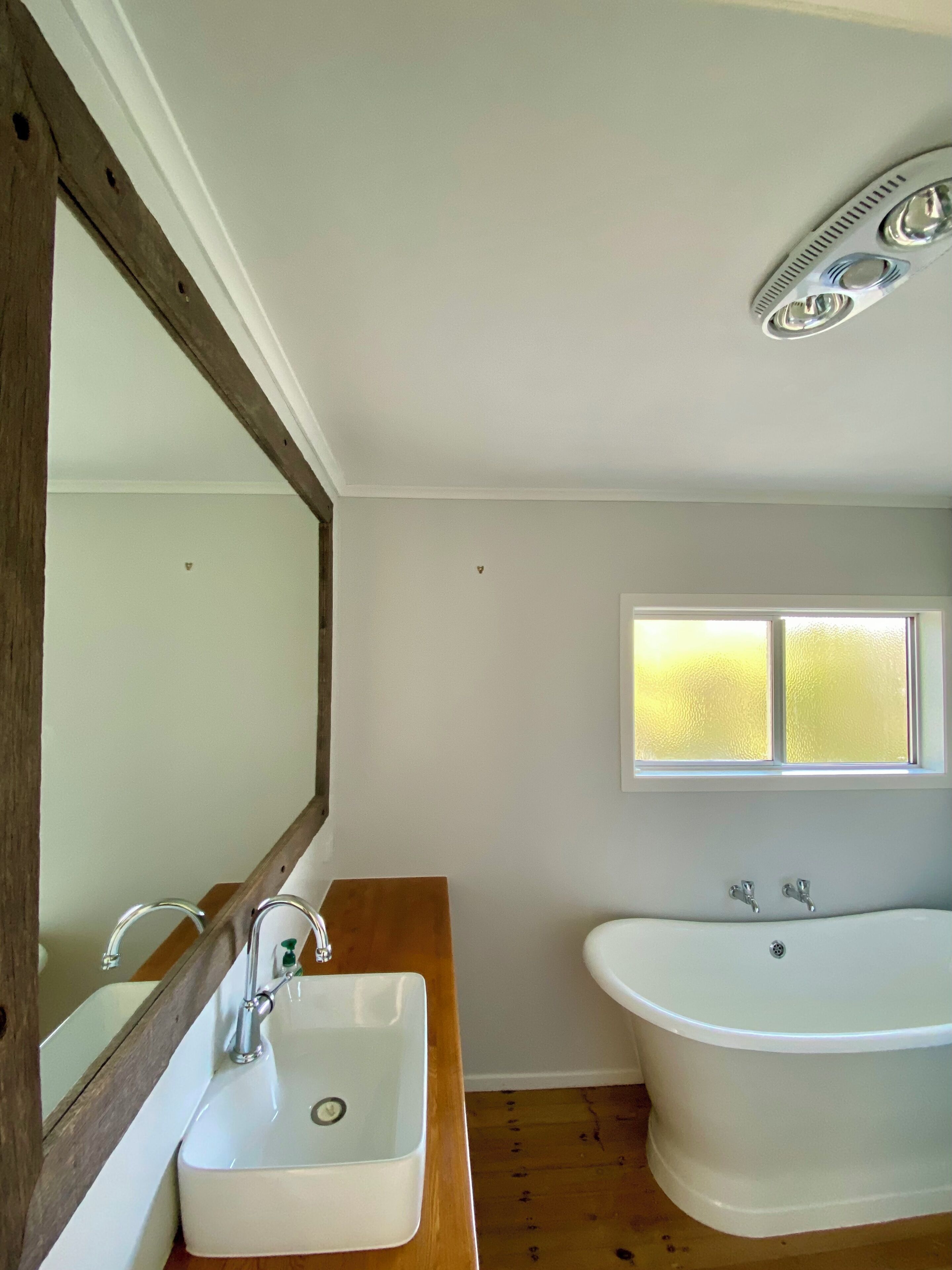 A bathroom with a wooden vanity, a white sink, a bathtub, a window, and a ceiling vent.