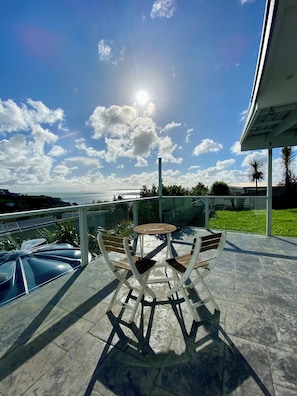 Un patio con mesa y sillas, barandilla de vidrio y vista al mar.