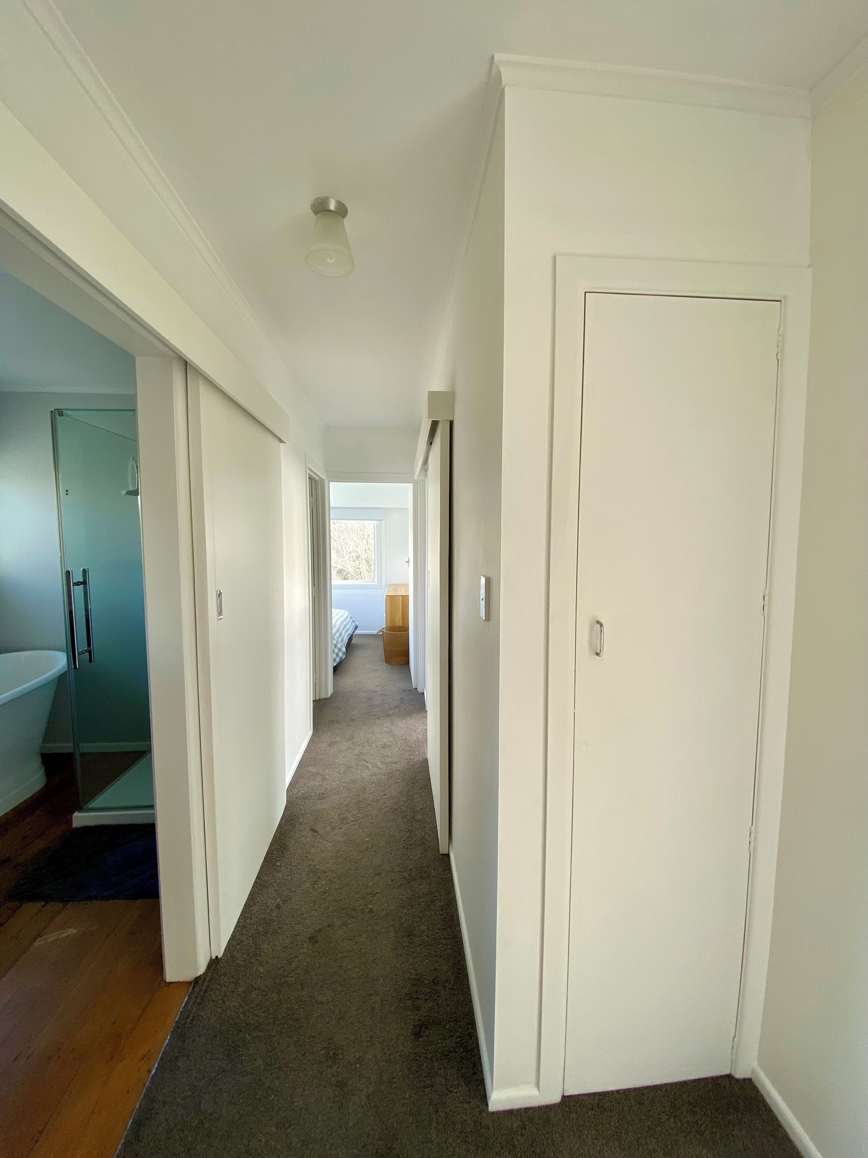 A hallway with white walls, a carpeted floor, and a door on the right.