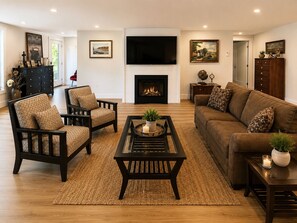 Un salon avec une cheminée, un canapé, deux fauteuils, une table basse et un téléviseur.