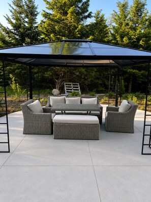 Un espace extérieur aménagé en patio, avec un coin salon couvert, une table et une échelle.