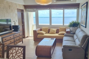 A living room with a sofa, TV, and a view of the sea. - Huge Lux. 2 BR Condo (100 SQM)  2 pools - Beach, Sea-views, Gym, Tours available (Lapu-Lapu City)