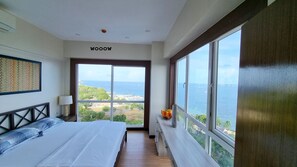 A bedroom with a bed, a nightstand, a lamp, a window with a view of the sea, and a wall with a 'WOOW' sign. - Huge Lux. 2 BR Condo (100 SQM)  2 pools - Beach, Sea-views, Gym, Tours available (Lapu-Lapu City)