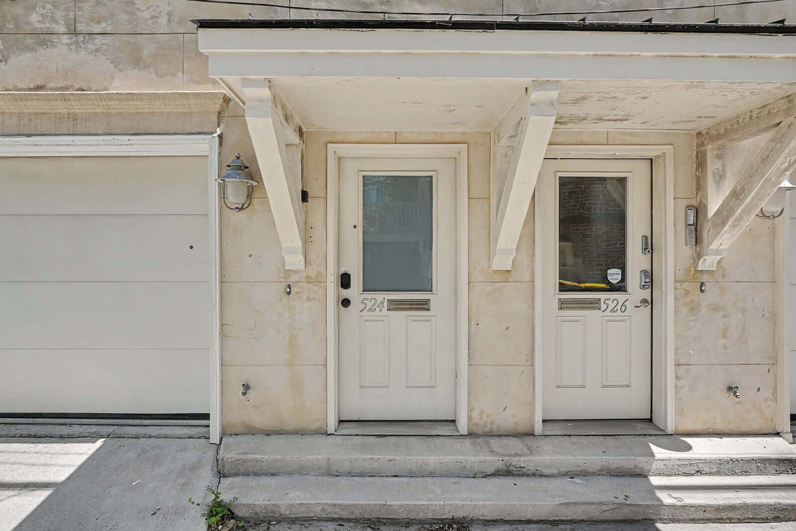 A residential building with two white doors marked with numbers 524 and 526, a garage door, and a small step leading to the entrance.