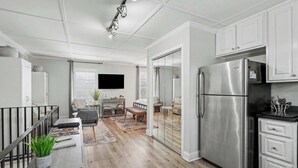 Una cucina moderna con frigorifero in acciaio inossidabile, mobili bianchi e un'area pranzo con tavolo e panca in legno.
