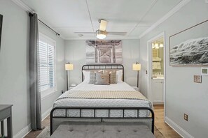 Ein Schlafzimmer mit einem Bett, Nachttischlampen, einem Deckenventilator, einem Fenster mit Jalousien und einer Tür zu einem Badezimmer.