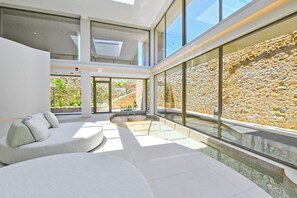 A modern interior with a curved seating area, large windows, and a stone wall. - Pearl Island Chios Hotel Spa (Chios)