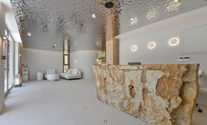 A modern reception area with a stone counter, white sofas, and a ceiling with a unique textured pattern. - Pearl Island Chios Hotel Spa (Chios)