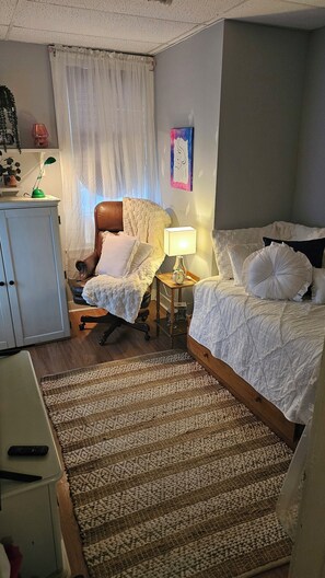 Una habitación de hotel con una cama, una silla, un escritorio, una lámpara y un cuadro en la pared.