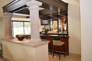 Uma área de bar com um pilar de pedra, banquetas, uma televisão e copos decorativos.