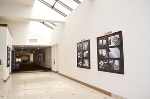Um corredor com claraboia, fotografias em preto e branco nas paredes e chão em mosaico.