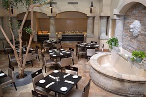 Een restaurant met gedekte tafels, een fontein en een stenen muur met een leoskulptuur.