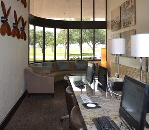 Um espaço de escritório moderno com uma escrivaninha curva, vários monitores, um laptop, um sofá e grandes janelas com vista para o exterior.