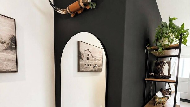Une pièce avec un mur d’accent de couleur noire, un miroir, une étagère avec des objets décoratifs et des œuvres d’art encadrées.