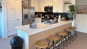Une cuisine moderne avec des meubles blancs, des appareils en acier inoxydable, un grand îlot central doté de tabourets et un panneau au-dessus de la porte.