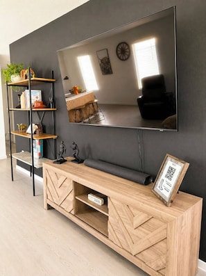 Een moderne woonkamer met een grote flatscreen televisie aan de muur, een houten tv-meubel eronder en een zwarte bank.