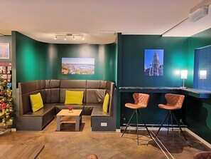 Un salon moderne avec un canapé d’angle, deux tabourets de bar, une table basse et une cheminée.