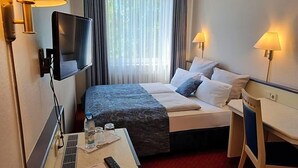 Quarto de hotel com uma cama, uma mesa, uma televisão e duas luminárias.