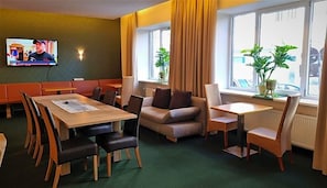 Ein Hotelzimmer mit Essbereich, einer Couch, einem Fernseher und großen Fenstern mit Vorhängen.