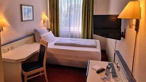Quarto de hotel com cama, escrivaninha, cadeira, televisão e janela com cortinas.