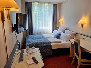 Une chambre d’hôtel avec un lit, un bureau, une télévision et deux lampes.