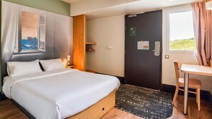 A hotel room with a bed, a desk, a chair, a window, and an air conditioning unit. - Hotel Premia Re Classe Roissy Saint Witz (Saint-Witz)
