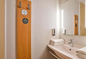 A bathroom with a wooden panel, a sink, a mirror, and a towel stack.