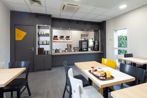 A modern cafe with a counter, seating area, and a view of greenery outside.