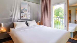 A hotel room with a large bed, a cityscape view through a window, a balcony with a view of greenery, and a door leading to another room. - Hotel Premia Re Classe Roissy Saint Witz (Saint-Witz)