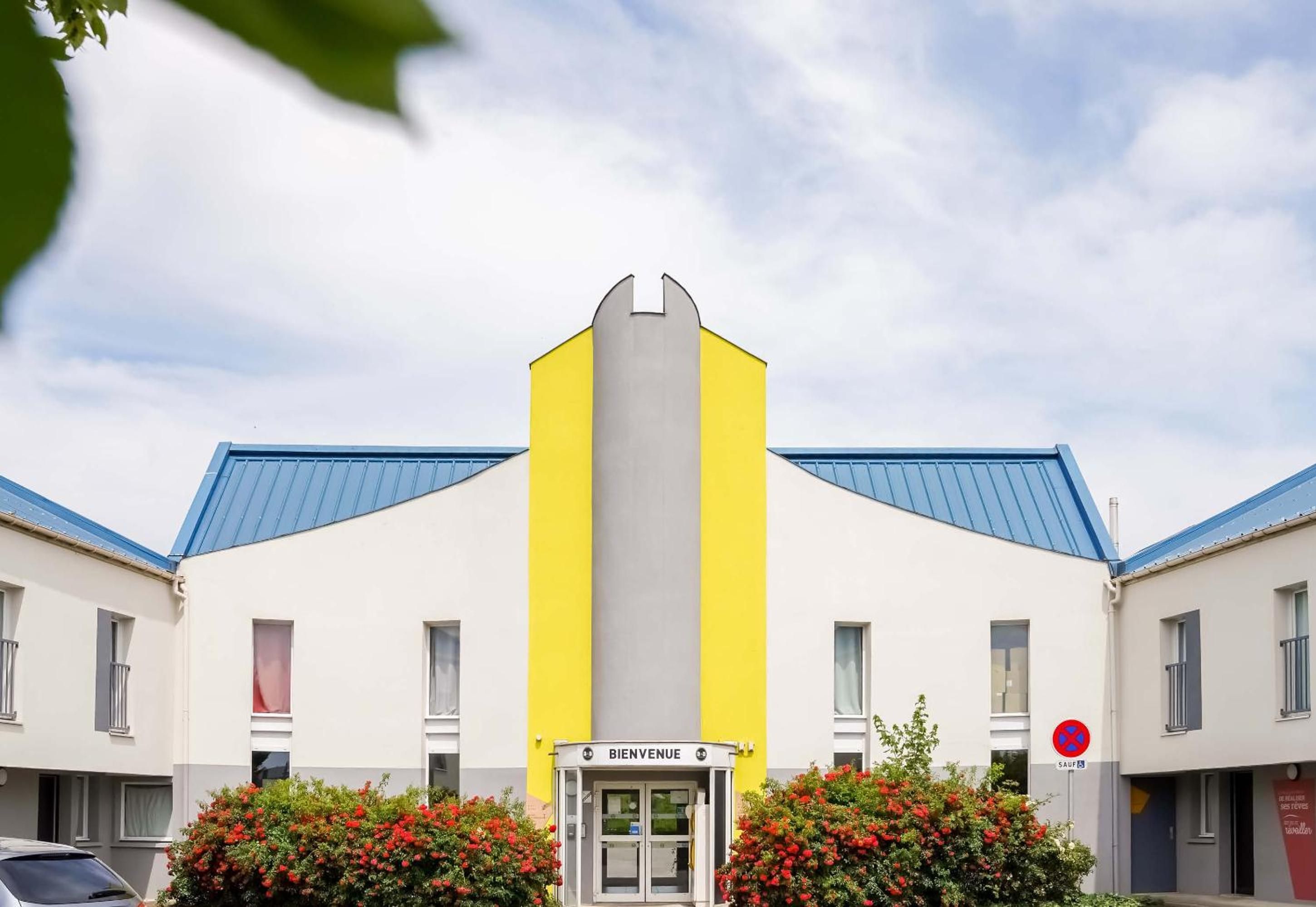 A building with a yellow and white facade, a blue roof, and a sign reading 'BIENVENUE'.
