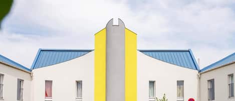 Un bâtiment à la façade jaune et blanche, avec un toit bleu et une enseigne sur laquelle on peut lire « BIENVENUE ».