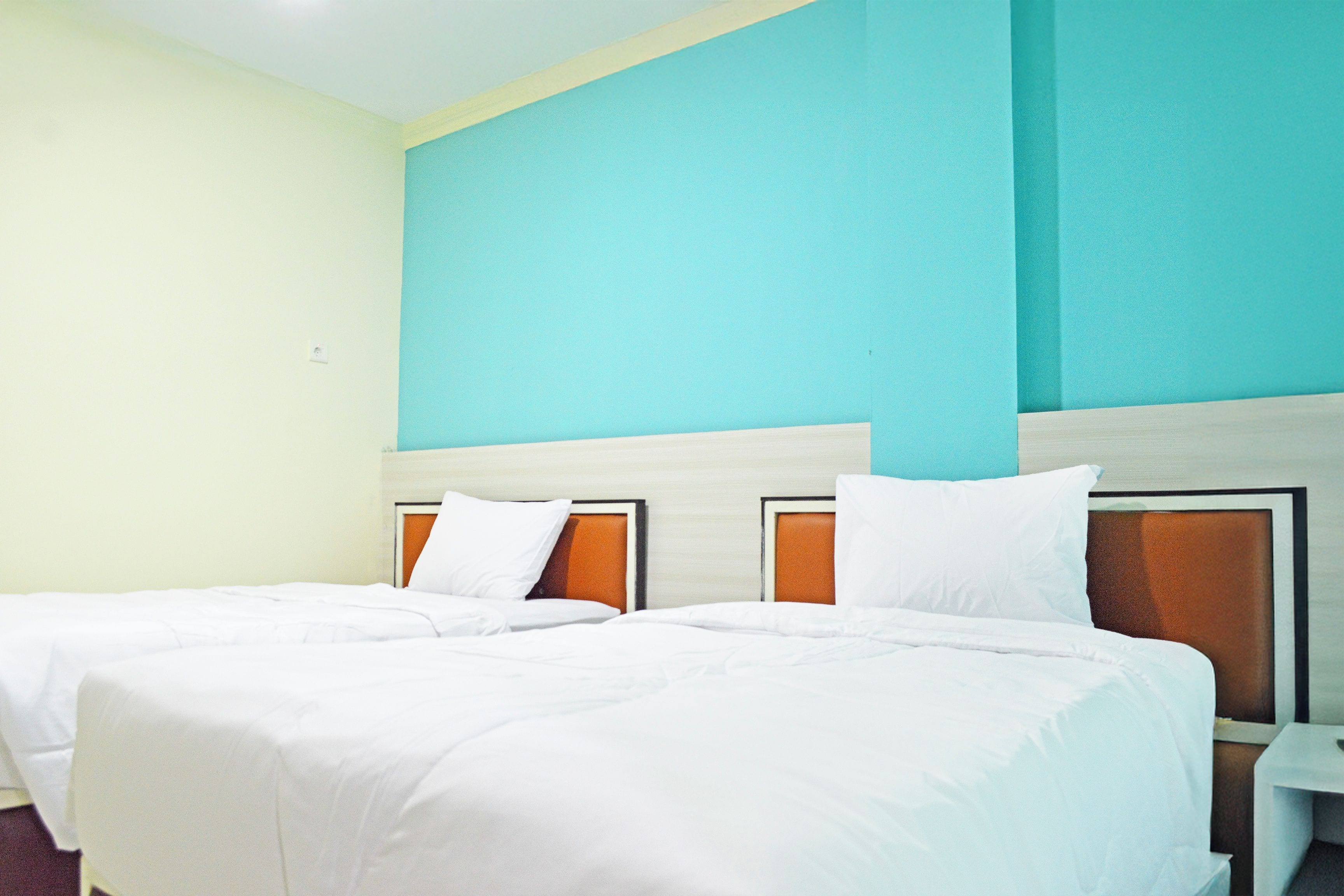 A hotel room with two beds, a wooden headboard, white bedding, and a teal accent wall.